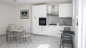 A modern kitchen with white cabinets, a gas stove, and a dining area with metal chairs.