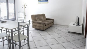 A room with a dining table, chairs, a sofa, a TV on a cart, and a painting on the wall.