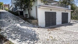 A cobblestone street leading to a building with two dark shutters and a balcony.