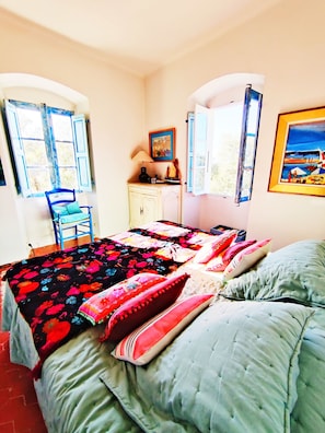 A bedroom with a bed, a chair, a dresser, and two windows with shutters.