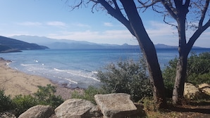 Eine Küstenlandschaft mit Strand, felsigem Vordergrund und Blick auf das Meer und entfernte Berge.