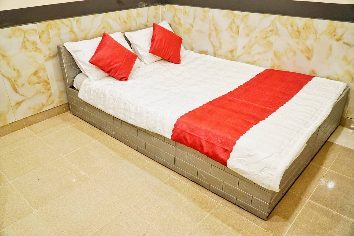 A neatly made bed with a grey headboard and white bedding, featuring red accents.
