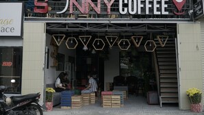 A coffee shop named 'Sunny Coffee' with a modern design, featuring hexagonal light fixtures and wooden crates outside. - Sunny Hostel (Can Tho)