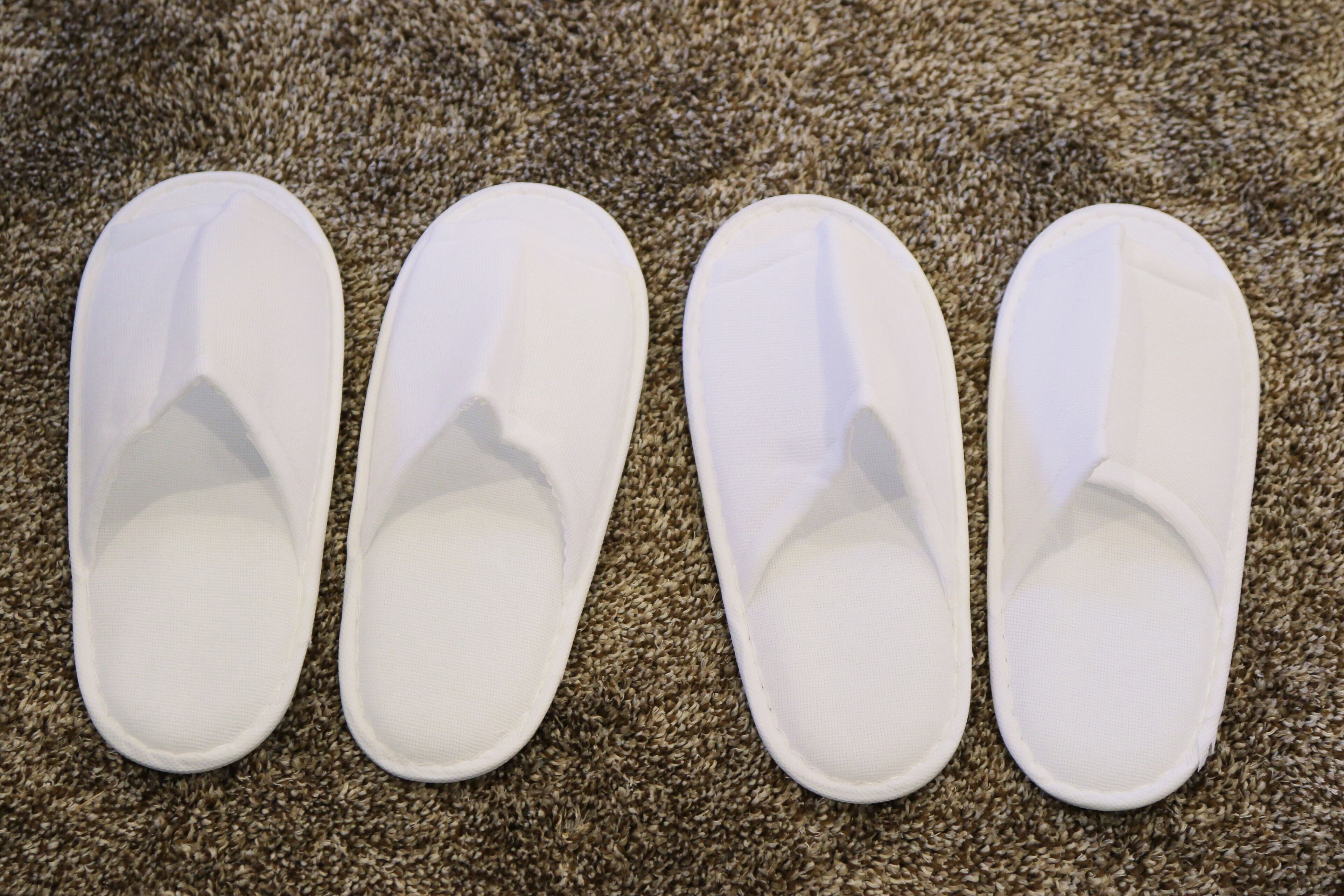 Cuatro pantuflas blancas sobre un piso alfombrado.