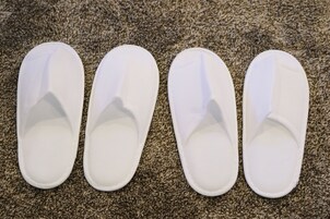 Cuatro pantuflas blancas sobre un piso alfombrado.