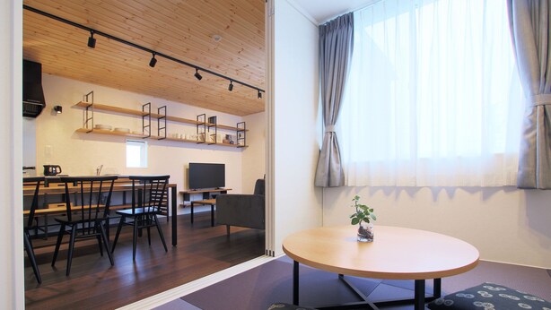Ein modernes Wohnzimmer mit Holzboden, einem runden Tisch und einer Couch mit gemusterten Kissen.