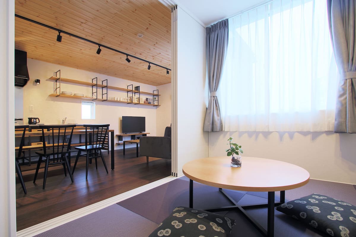 A modern living room with a wooden ceiling, a round table, and a sofa with patterned cushions.