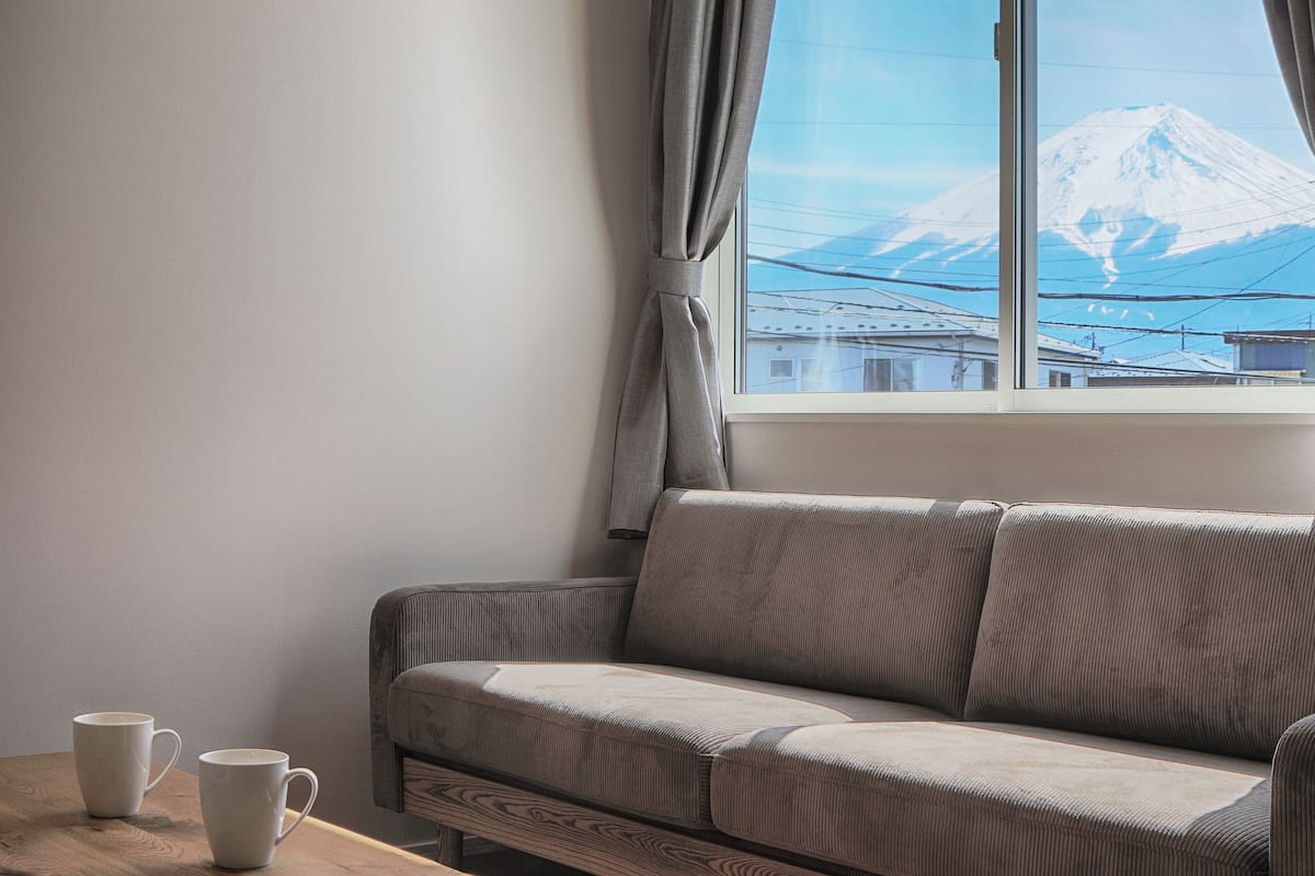 A room with a sofa, two white mugs on a wooden table, and a view of a snow-capped mountain through a window.