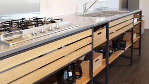 Eine moderne Küche mit einer Edelstahl-Arbeitsplatte, Hollauszügen und einem eingebauten Gasherd.