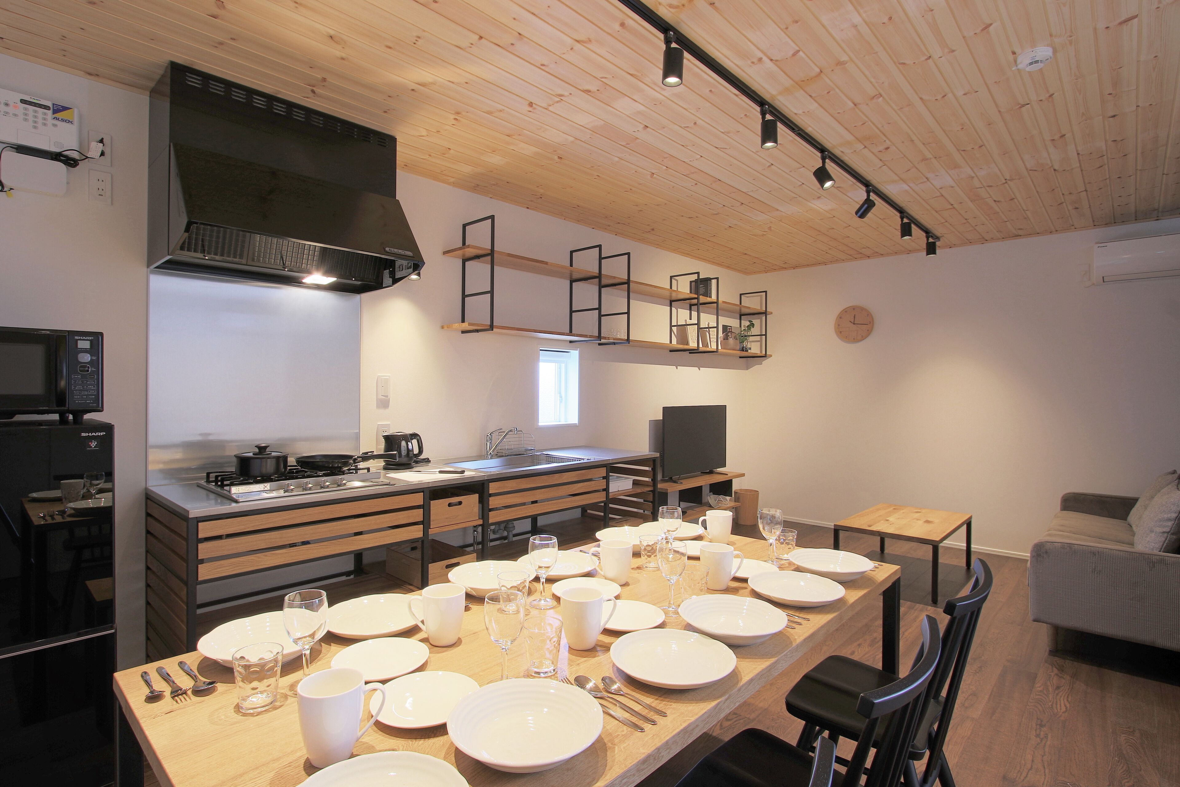 A modern kitchen with wooden cabinets, a built-in stove, and a dining area set for six with white plates and glasses.