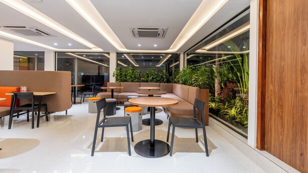 Un espace intérieur moderne, aménagé avec des coins salon comprenant des tables et des chaises, et doté d’une grande fenêtre offrant une vue sur la verdure environnante.