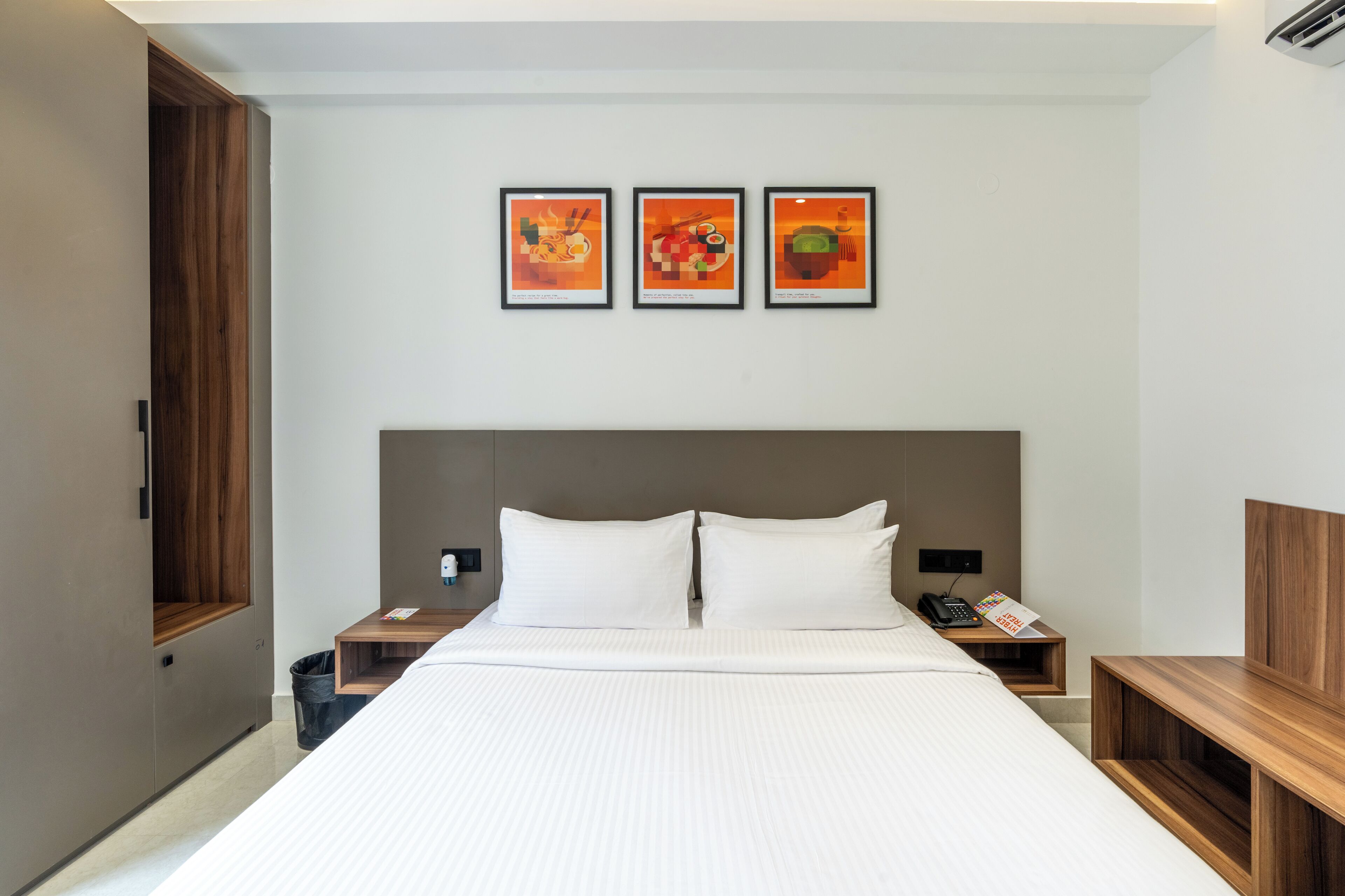 A hotel room with a large bed, two bedside tables, a wooden headboard, and three framed artworks on the wall.