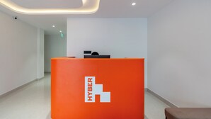 Un espace d’accueil doté d’un bureau orange vif orné du logo « HYBER », d’un design de plafond moderne et d’un intérieur épuré et minimaliste.