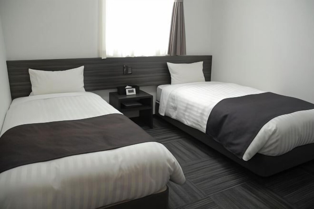 A hotel room with two beds, a nightstand, and a window with curtains.