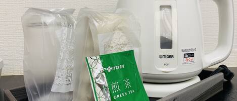 Een witte elektrische waterkoker, twee heldere plastic zakken en een groen pakje met de tekst 'GREEN TEA' op een zwarte dienblad.