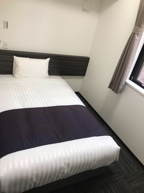A hotel room with a large bed, a dark headboard, a window with curtains, and a wall-mounted thermostat. - Okachimachi Urban Hotel (Tokyo)
