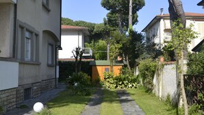 A courtyard with a stone pathway, a large tree, and a building with a balcony. - Villetta Adriana, indipendente spaziosaluminosa (Lido di Camaiore)