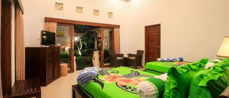 A bedroom with a green bedspread, a TV, a bench, and a view of the outdoors.