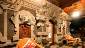 A traditional building with carved stone doors and walls, a wooden ceiling, and a seating area with a chair and a cushion. - Asli Bali Villa (Bangli)
