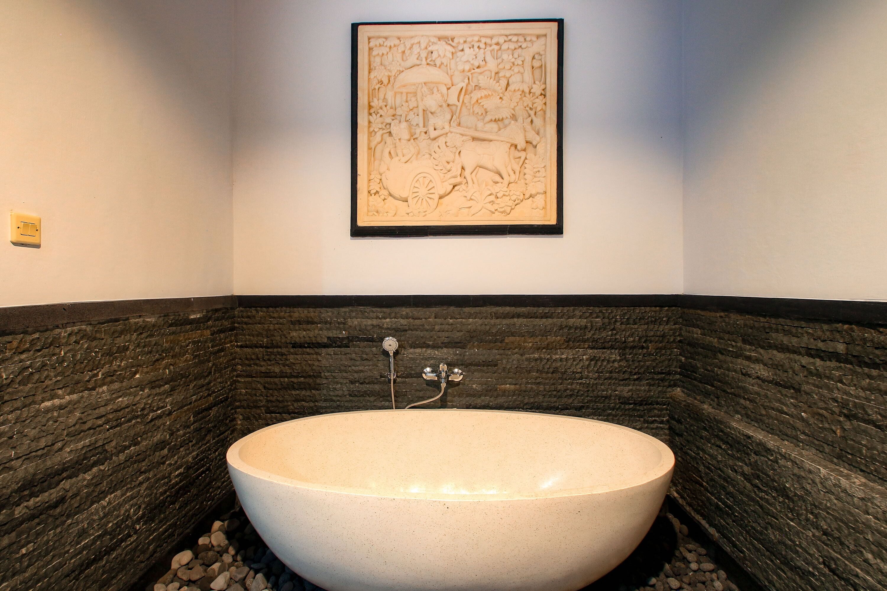 A bathroom with a freestanding bathtub, a stone wall, and a framed artwork above the tub.