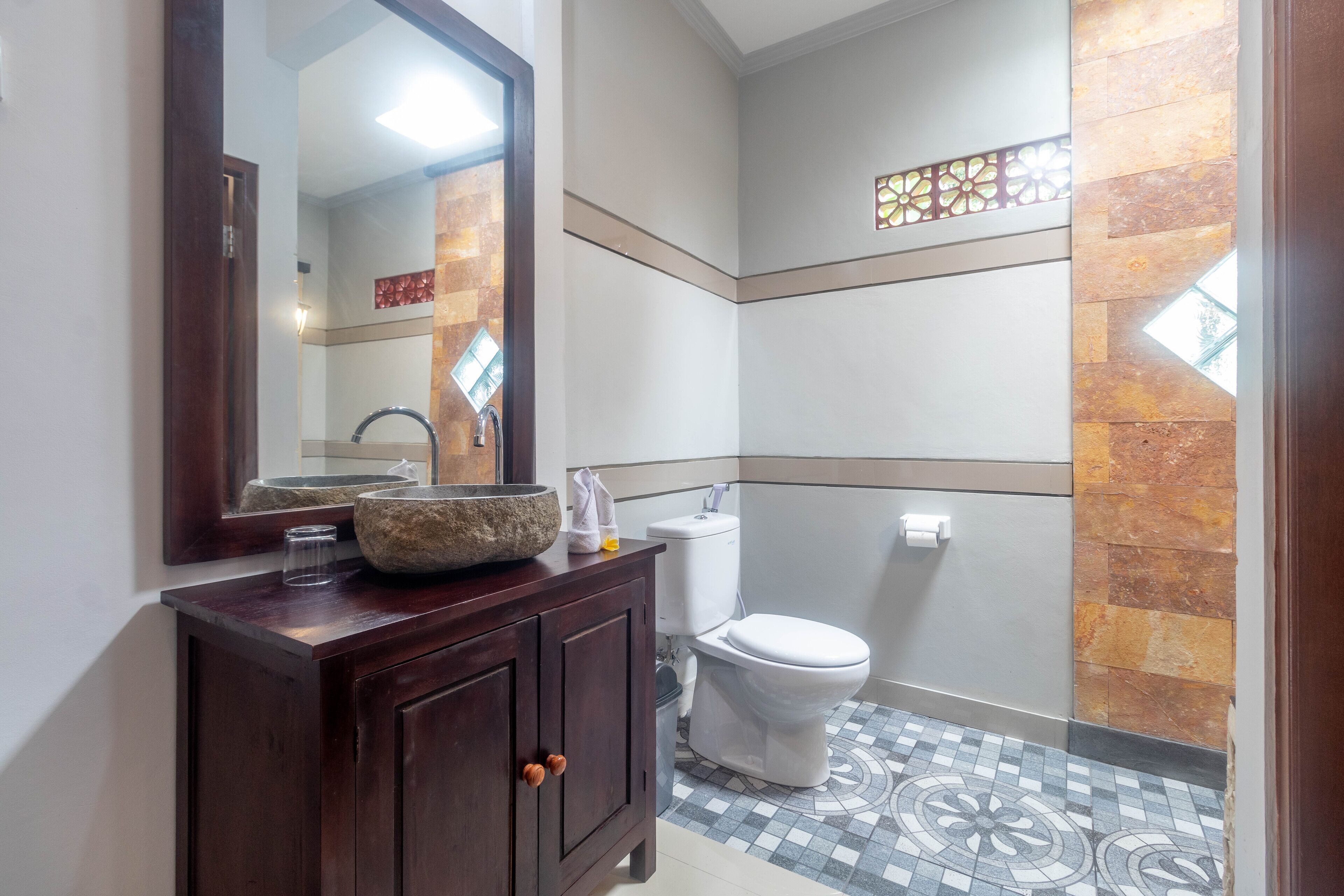 Une salle de bain avec un meuble-lavabo en bois, un grand miroir, des toilettes blanches et un carrelage à motifs.