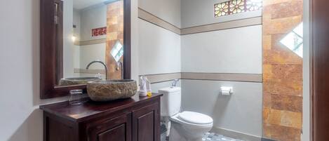 Une salle de bain avec un meuble-lavabo en bois, un grand miroir, des toilettes blanches et un carrelage à motifs.
