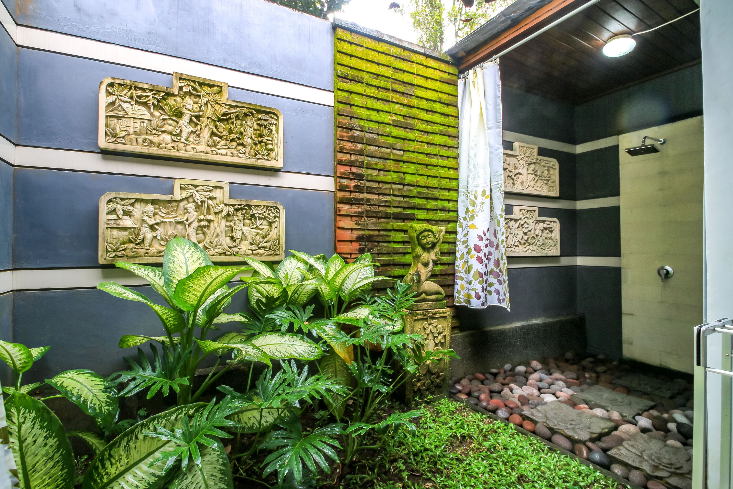 A bathroom with a shower, a decorative wall with carvings, and lush green plants.