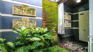 A bathroom with a shower, a decorative wall with carvings, and lush green plants.