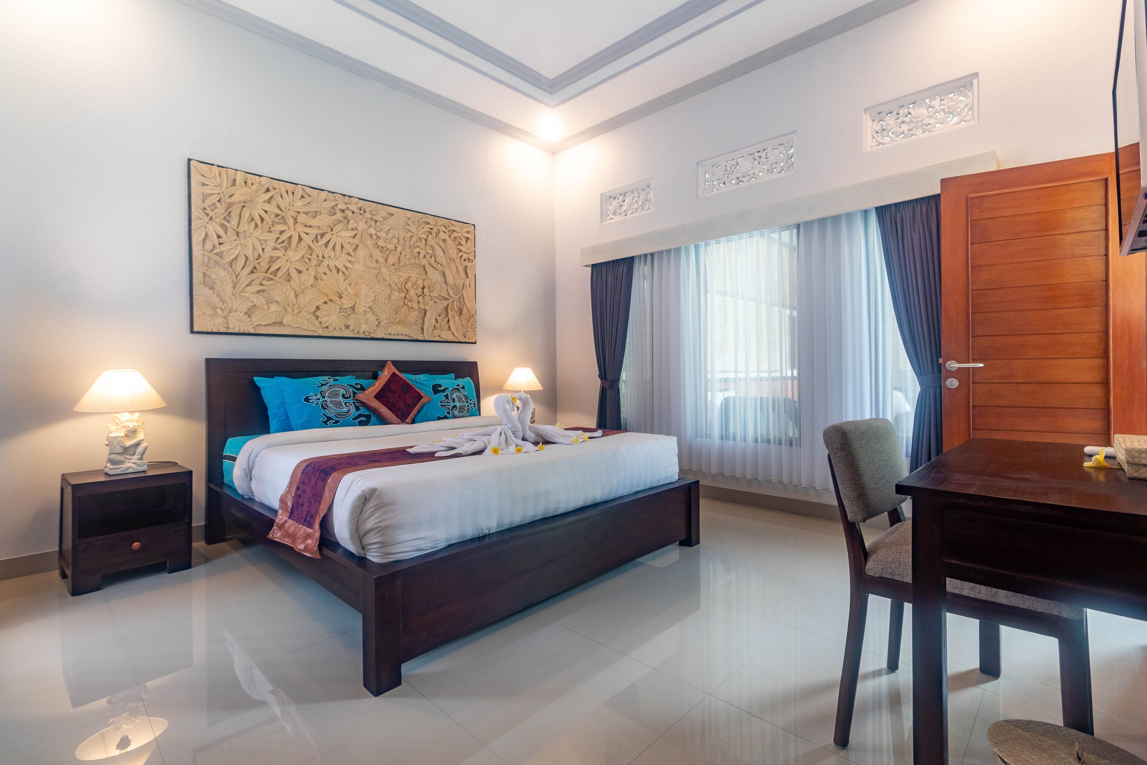 A hotel room with a large bed, two bedside tables with lamps, a wooden desk, and a large window with curtains.