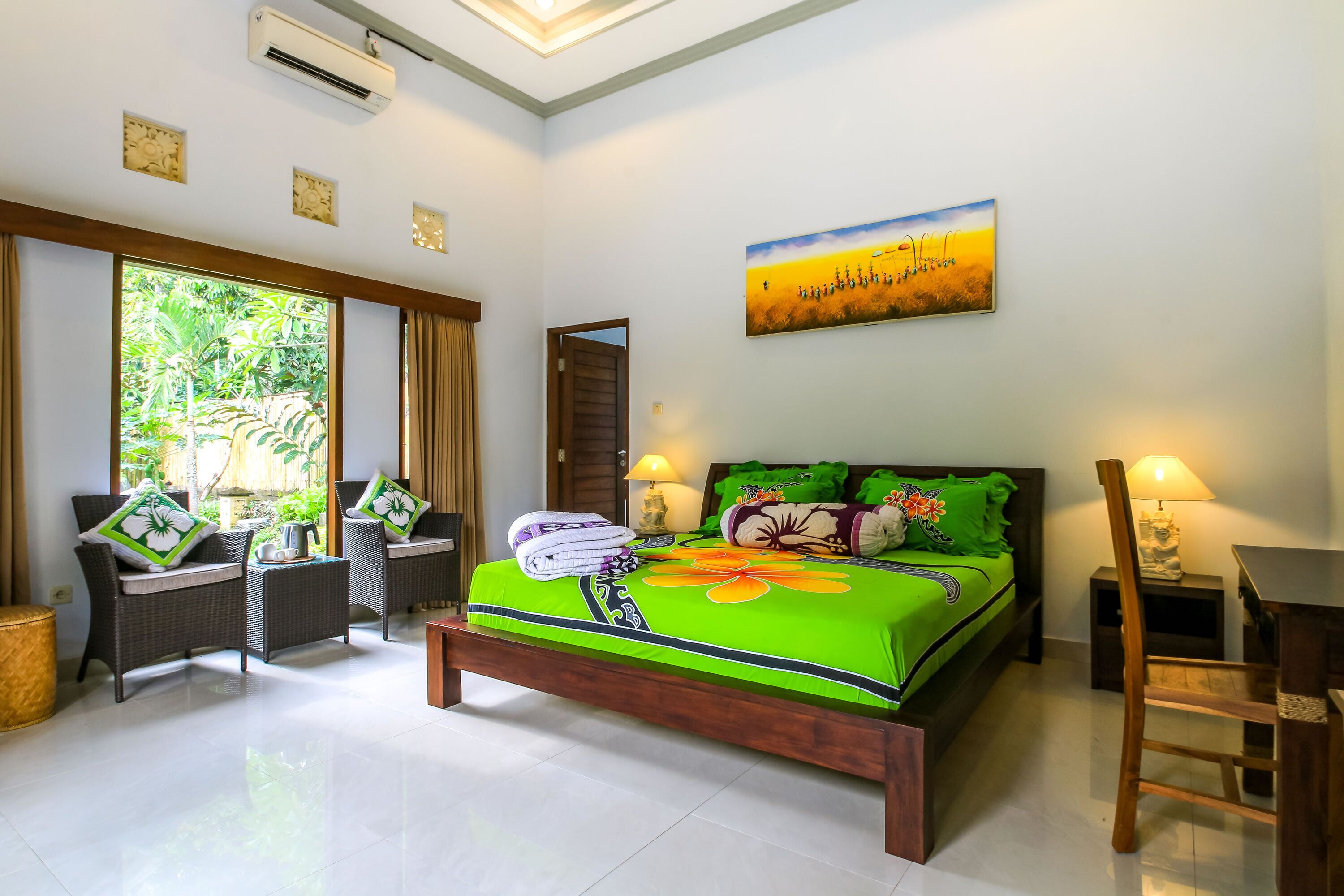 A bedroom with a large bed, two chairs, a wooden table, and a painting on the wall.