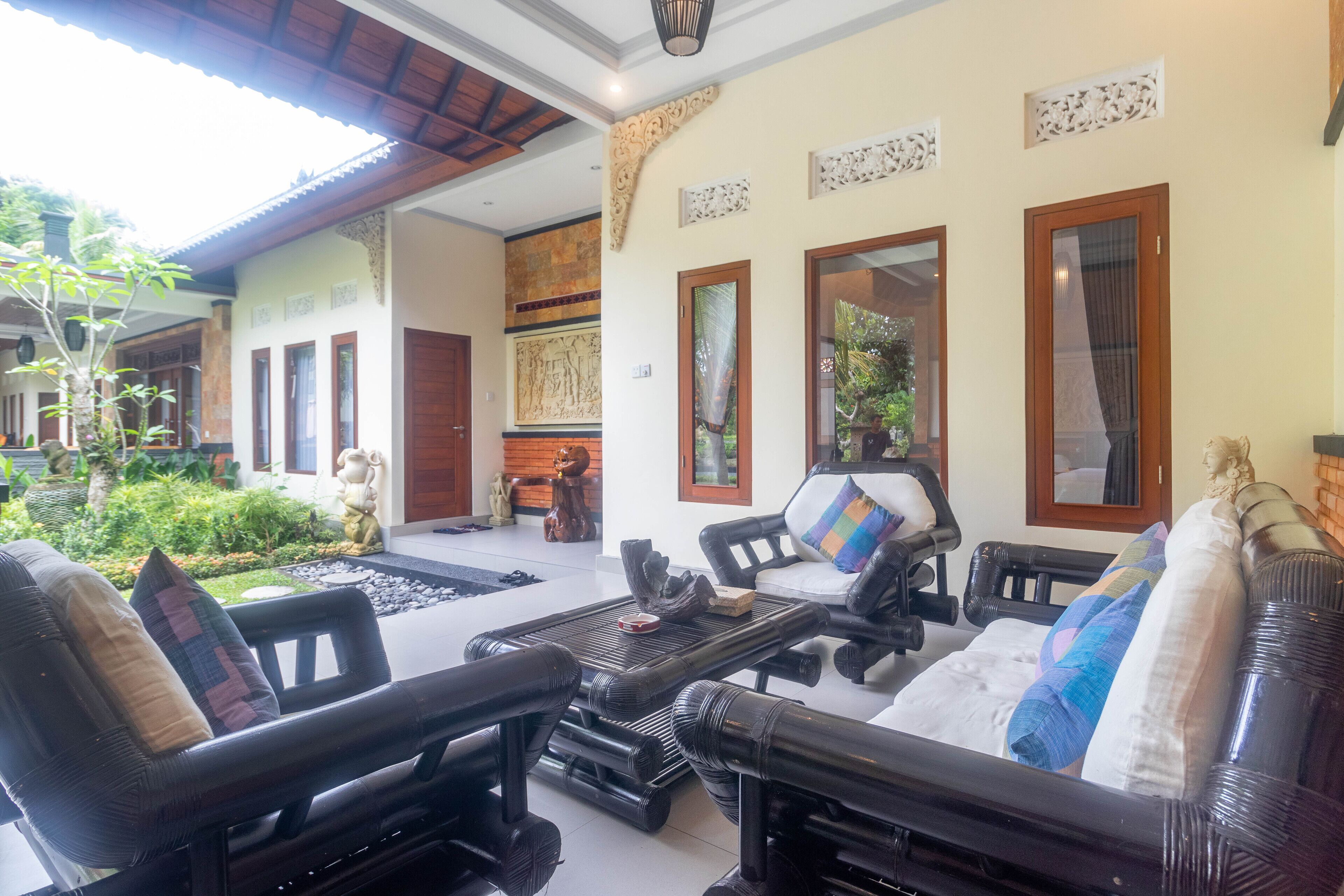 A spacious living area with a large sofa set, a coffee table, and a dining table. There are decorative wall panels and a view of the garden outside.