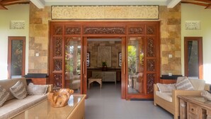 A spacious living area with a large wooden door, wicker furniture, and a fireplace. - Asli Bali Villa (Bangli)