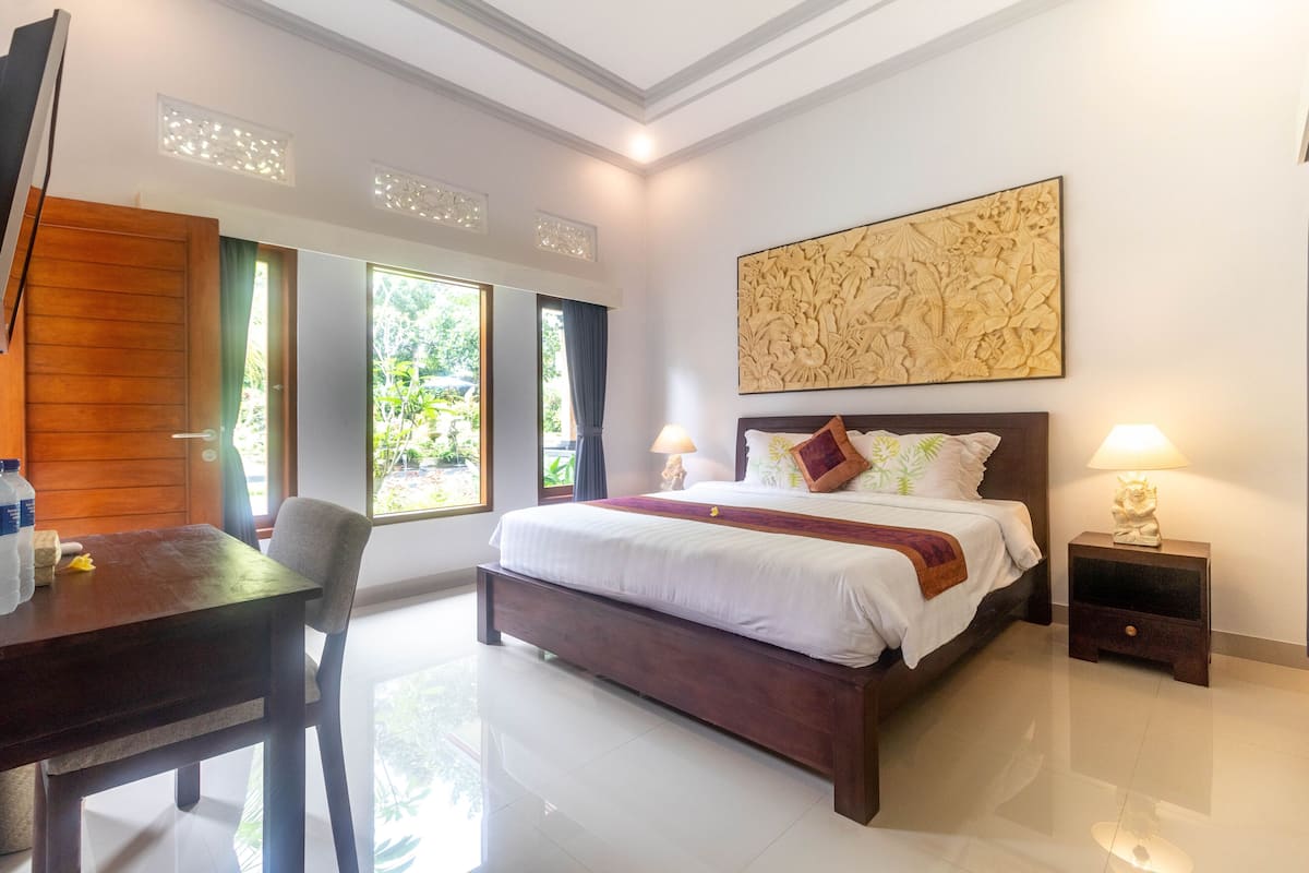 A hotel room with a bed, bedside lamps, a wooden desk, and a large window.