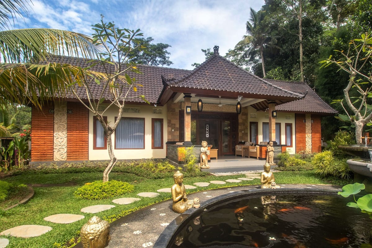 A traditional house with a tiled roof, a front garden with a pond, and statues.