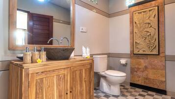 A bathroom with a wooden vanity, a large mirror, a sink with a stone basin, a toilet, and a decorative wall panel.