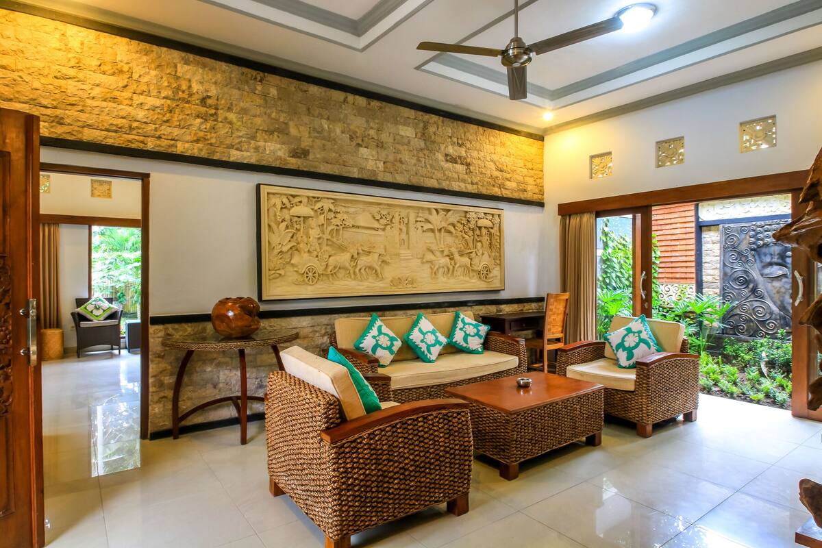 A spacious living area with wicker furniture, a ceiling fan, and a large wall mural.