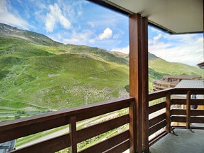 A balcony with a view of a mountainous landscape, a road, and a building with a sloped roof. - Cozy apartment in Menuires - Sleeps 4, wifi included (Les Menuires)