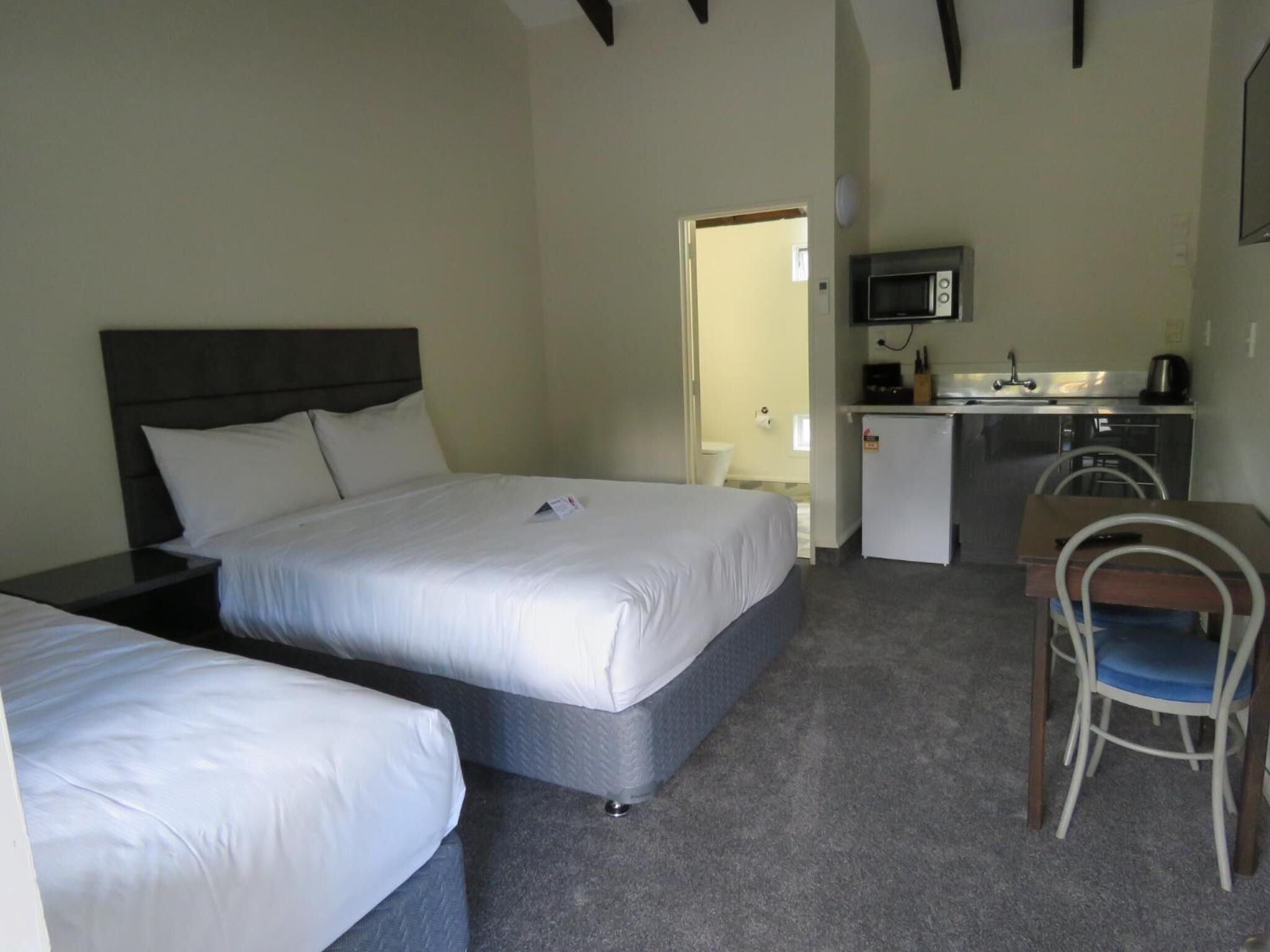 A hotel room with two beds, a small kitchenette, and a single chair.