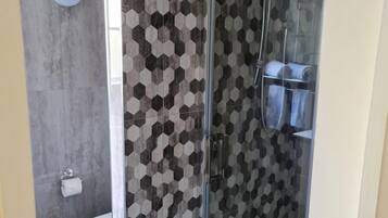 A modern bathroom with a glass-enclosed shower, a toilet, and a patterned hexagonal tile wall.