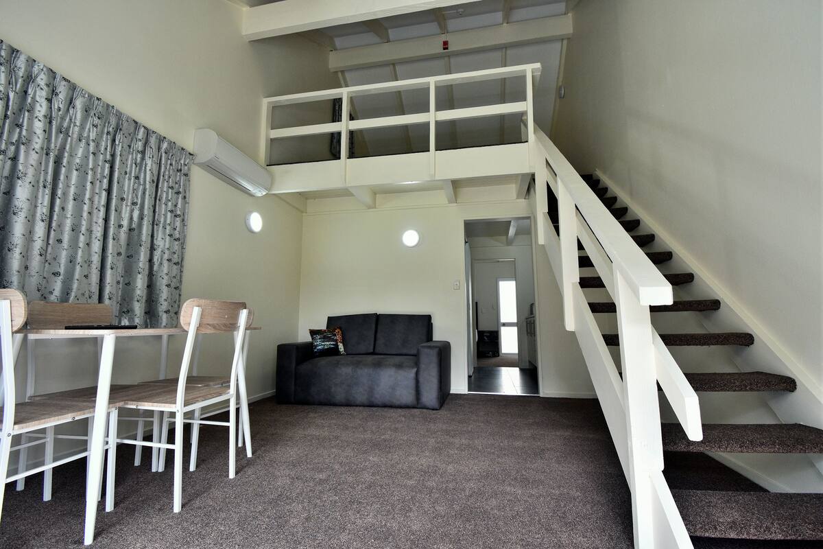 Un espace de vie compact comprenant un coin repas, un canapé, un escalier et un ventilateur de plafond.