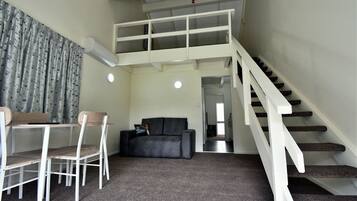 A compact living space with a dining area, a sofa, a staircase, and a ceiling fan.
