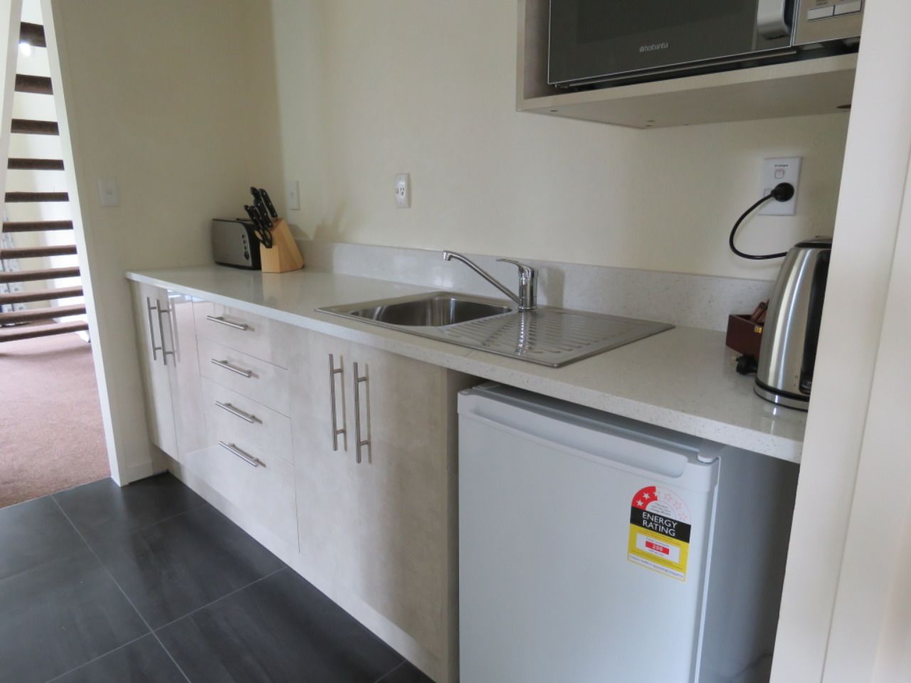 A compact kitchen with a built-in sink, a small refrigerator, and a microwave above the counter.