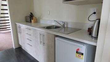 A compact kitchen with a built-in sink, a small refrigerator, and a microwave above the counter.