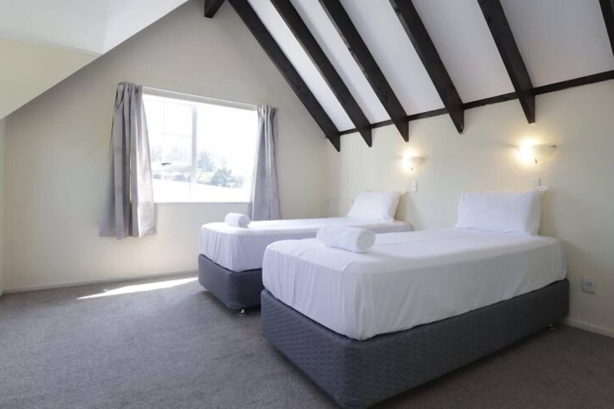 Une chambre avec deux lits, une fenêtre et un plafond en pente avec des poutres apparentes.