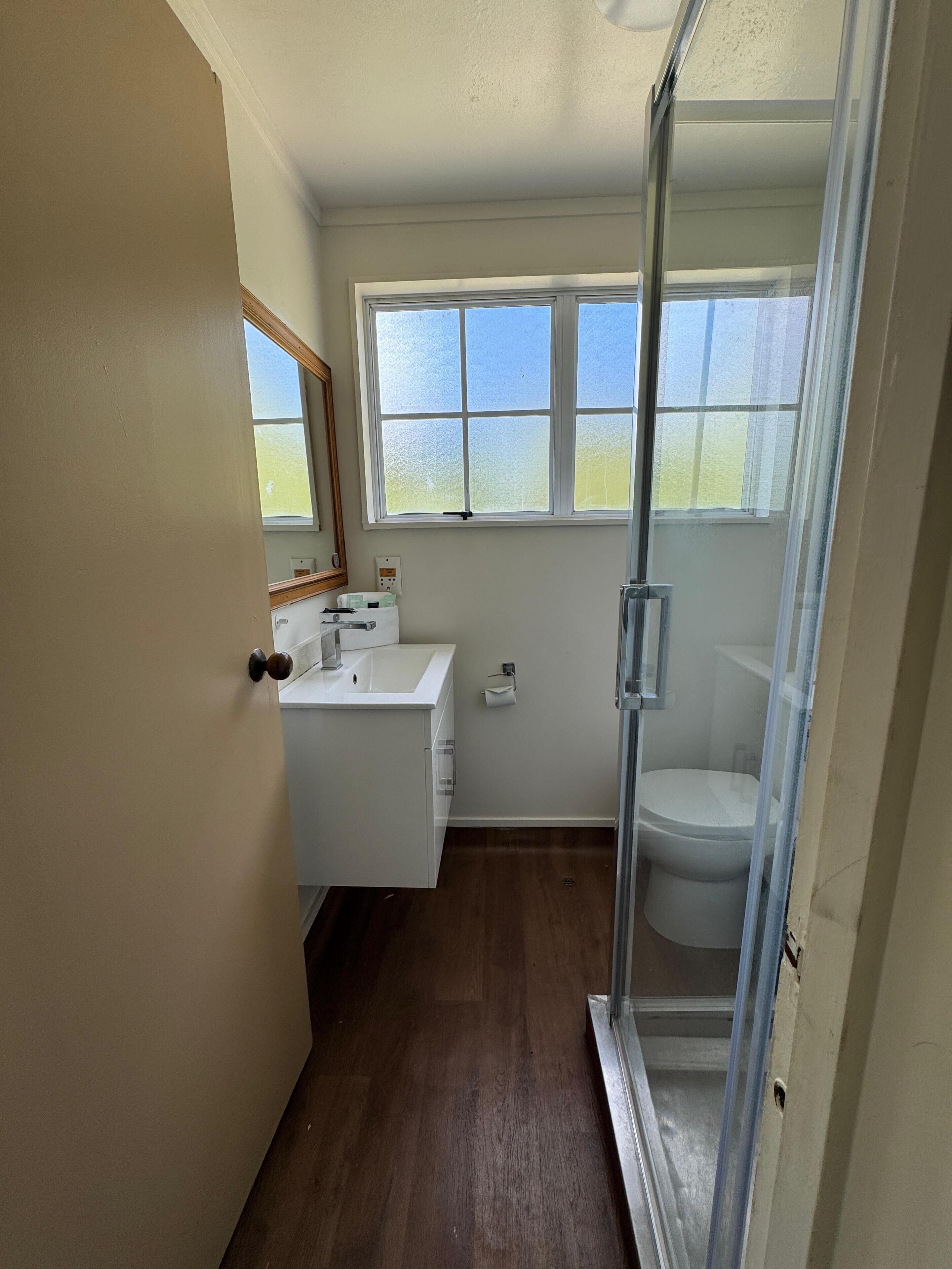 A bathroom with a wooden floor, a white sink, a toilet, and a glass shower enclosure.