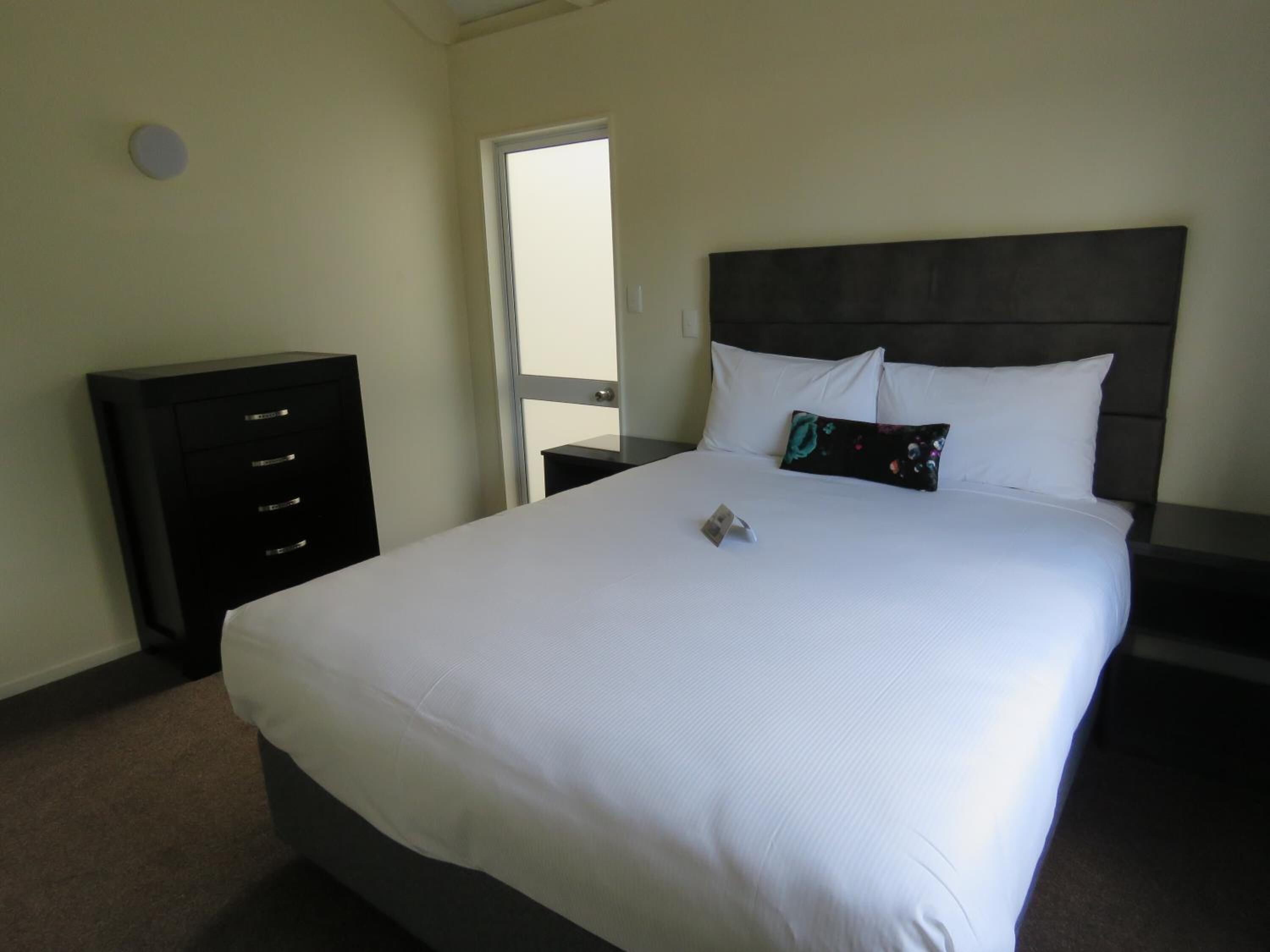 A hotel room with a large bed, a dresser, and a door leading to a balcony.