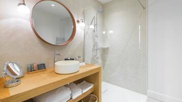 A modern bathroom with a round mirror, a wooden vanity, a white sink, and a glass-enclosed shower.