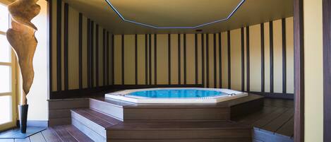 A modern indoor hot tub with a geometric ceiling design, wooden steps, and a vertical striped wall.