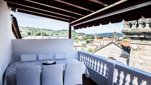 Un balcó amb taula i cadires, que ofereix vistes a un paisatge urbà amb edificis històrics i zones verdes.