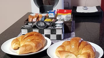 Dos platos de cruasanes sobre una encimera de cocina con una cafetera y varios alimentos al fondo.